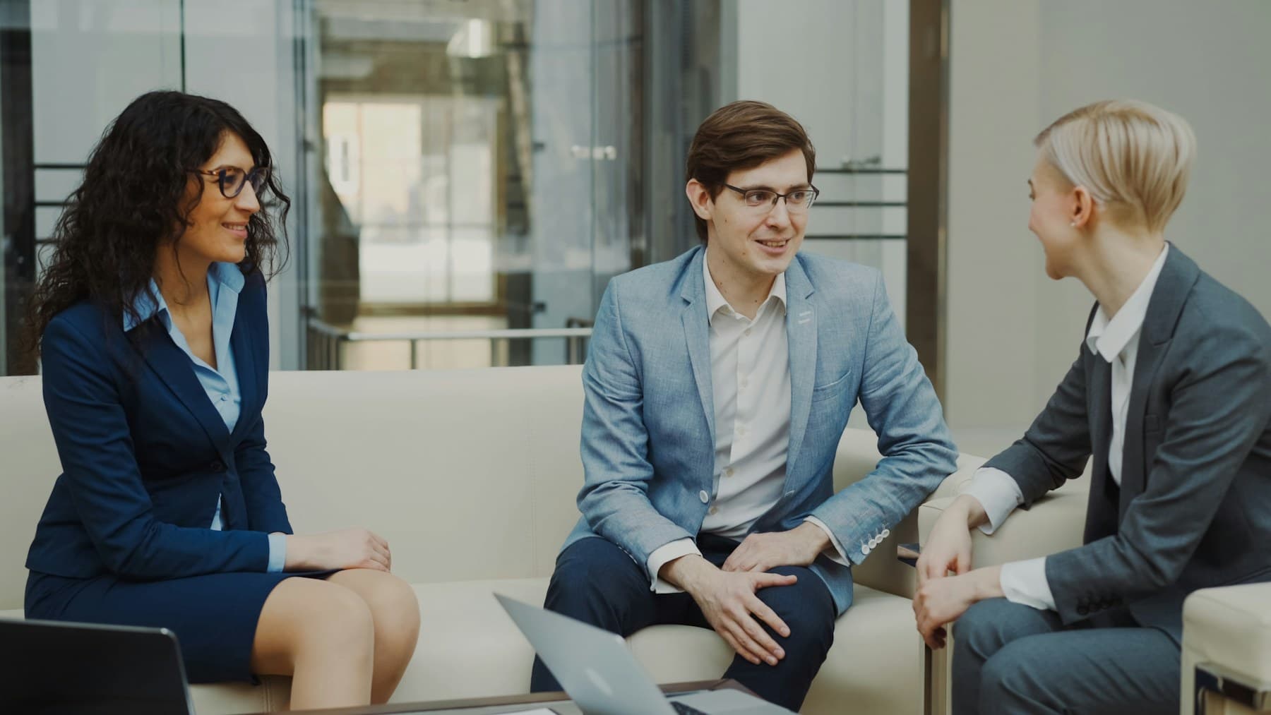 Three colleagues in conversation on lounge seating off the main office floor.