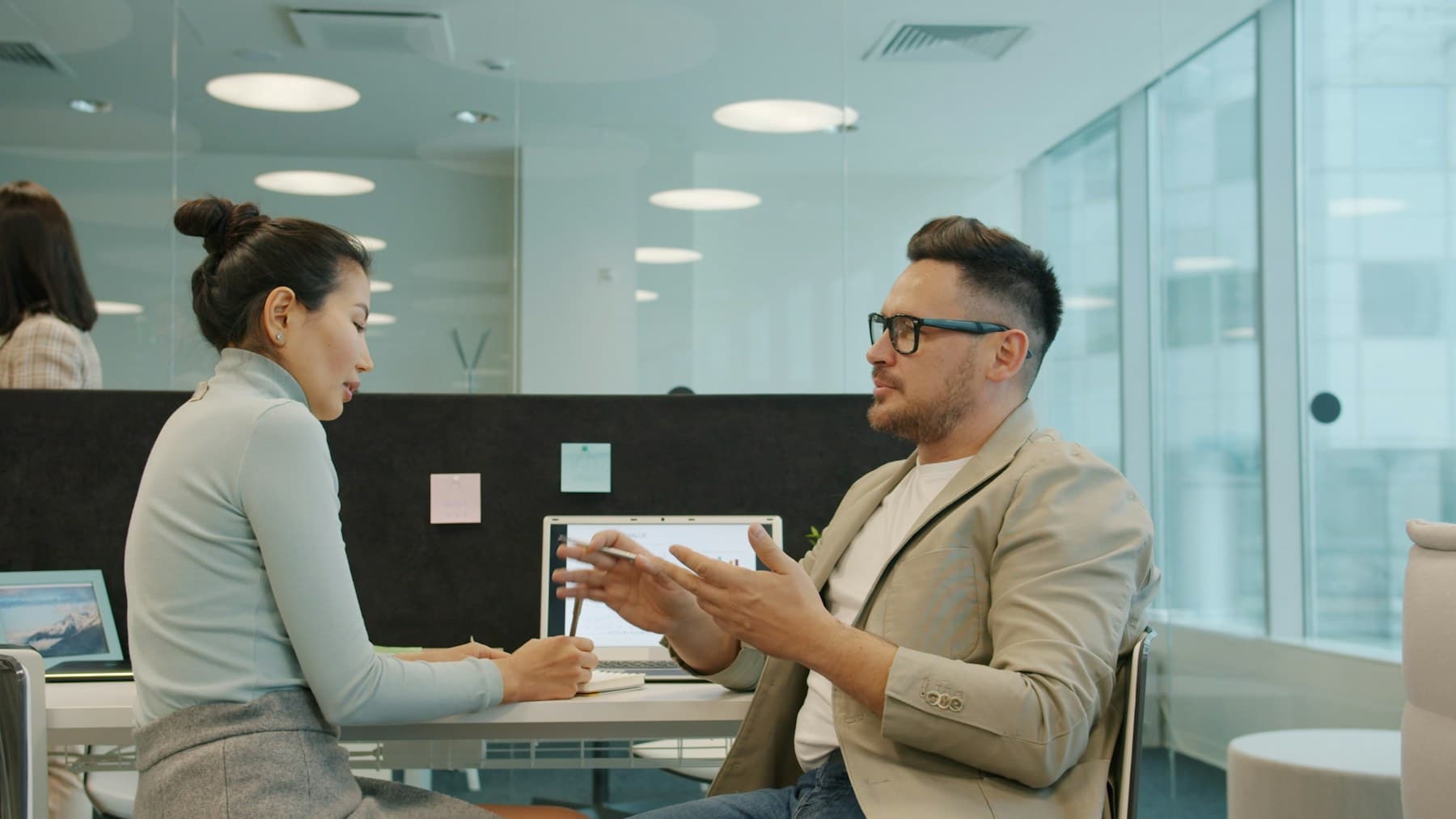 Two colleagues at a desk mid-conversation, one making a point with both hands.