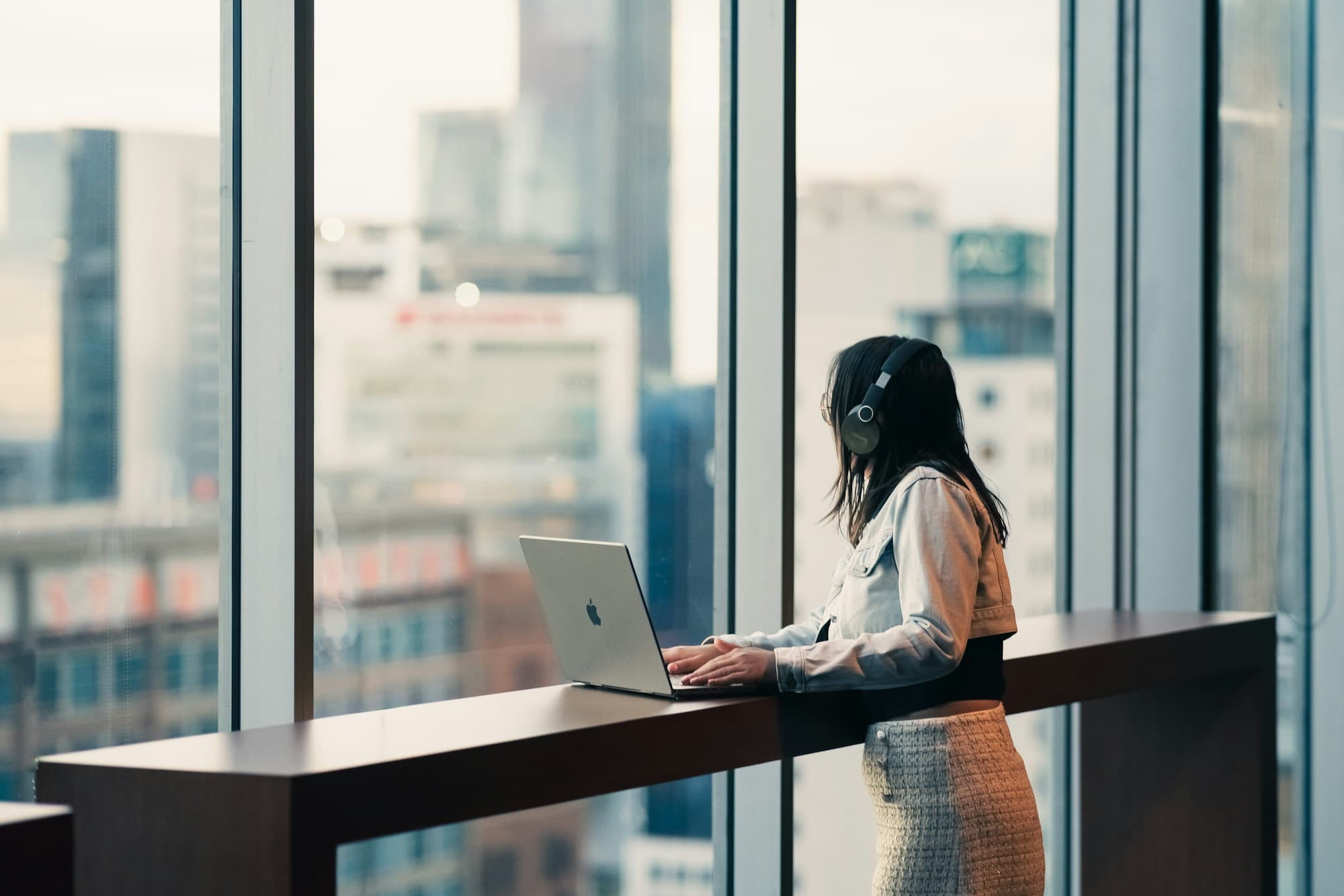 A sales rep working at a standing rail along a window wall, headset on, the city skyline behind them.