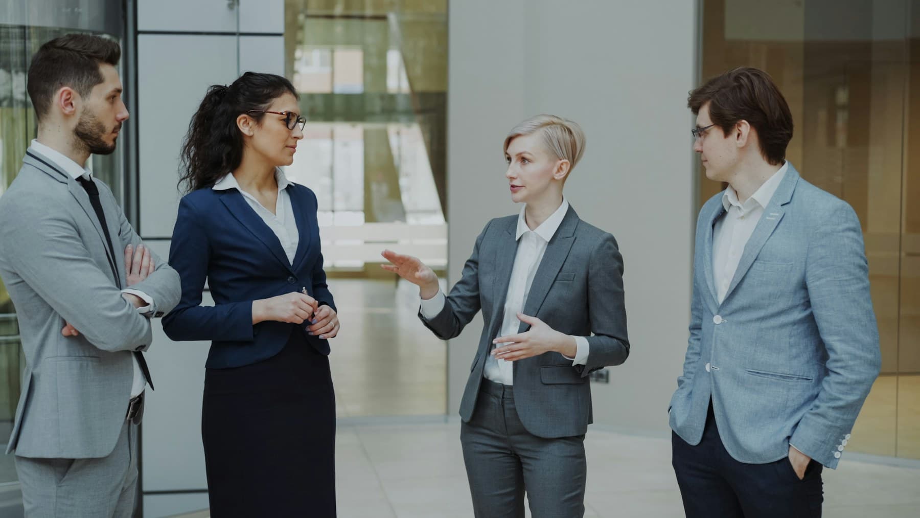 Four colleagues in business dress around a desk, one standing, working through a brief together.